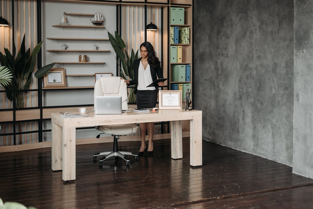 Confident professional woman in a modern office environment standing by a desk, suggesting leadership and success.